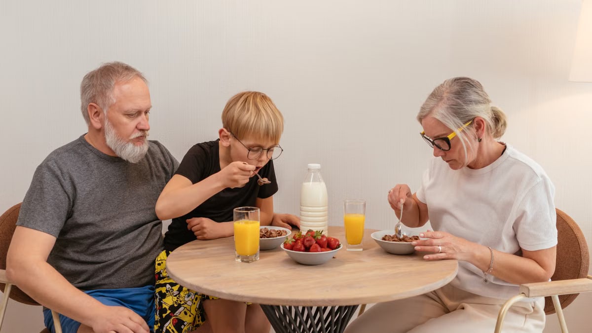 A family of three enjoying breakfast around a wooden table at home.